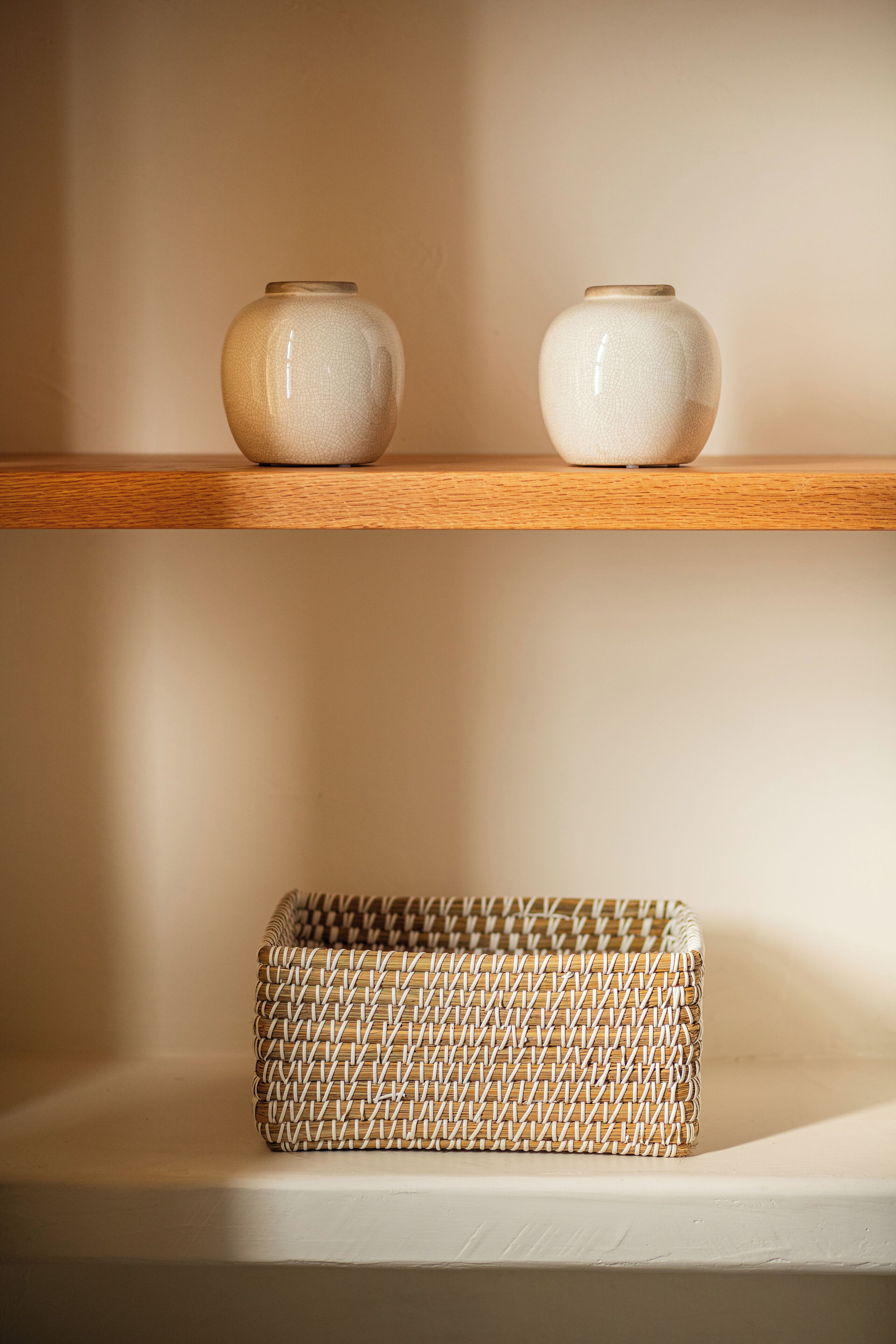 Two ceramic vases on a wooden shelf and a woven basket on a lower shelf.