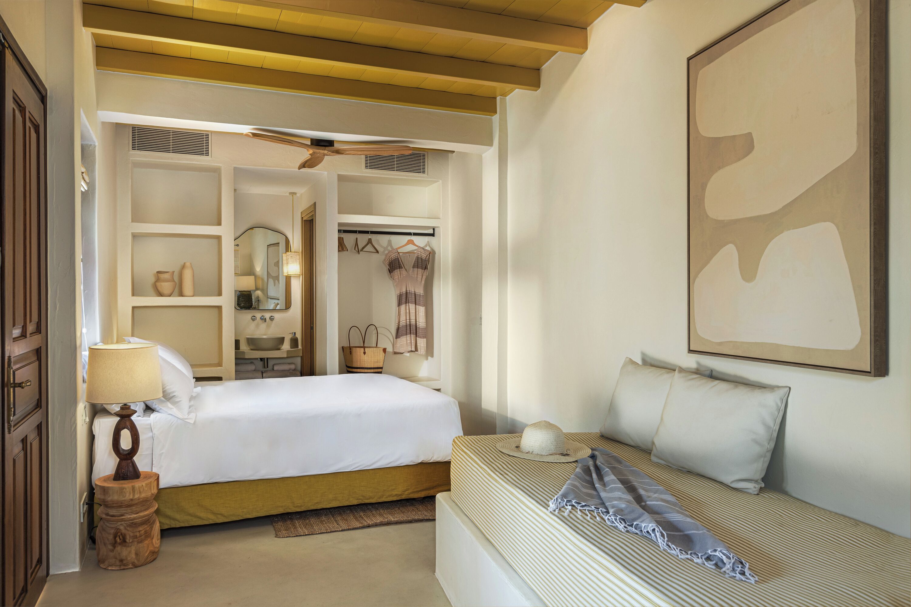 A bedroom with a bed, bedside table, lamp, and a large abstract painting on the wall.