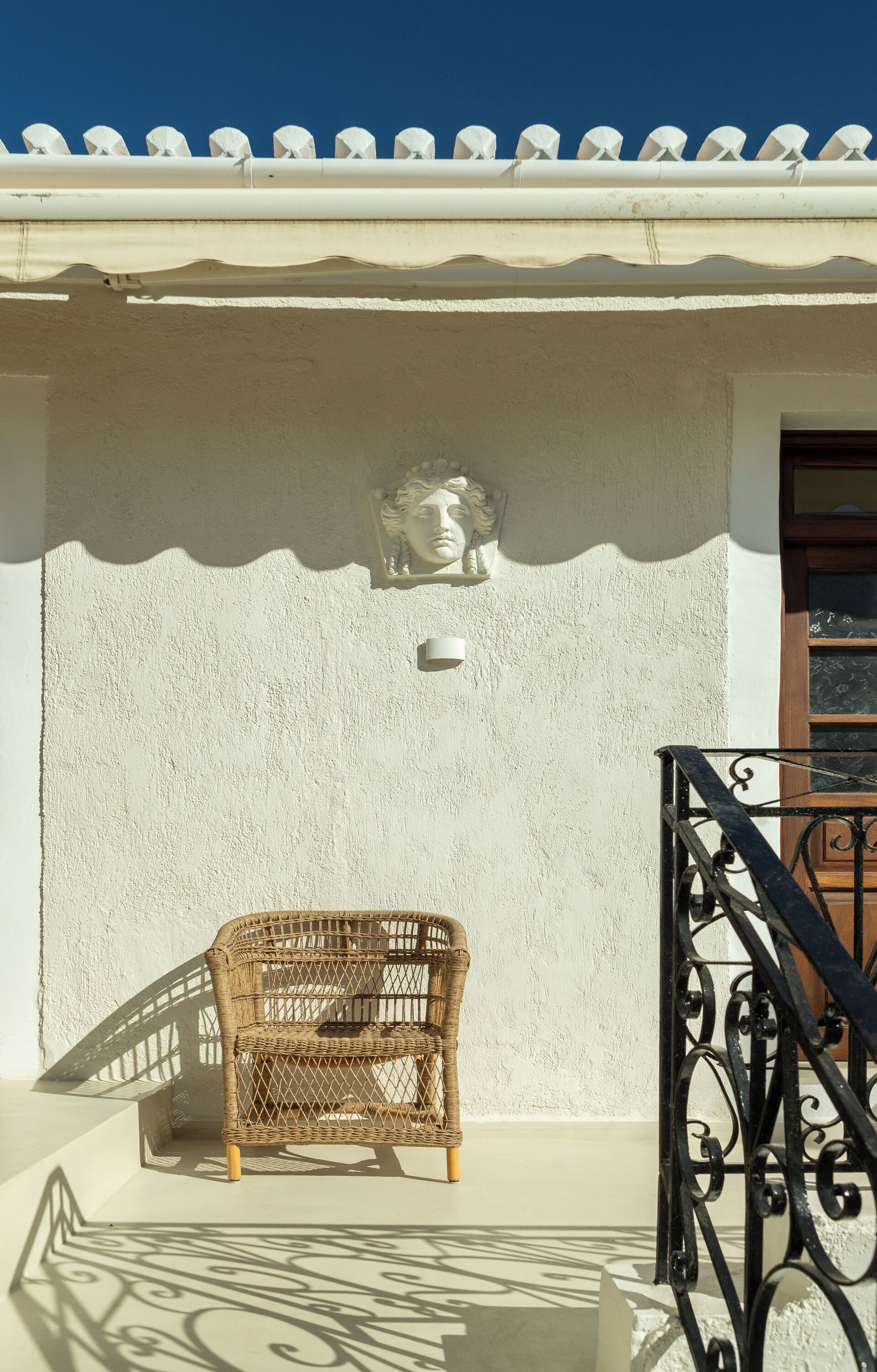 Una silla de mimbre en un balcón con una pared blanca y un techo decorativo.