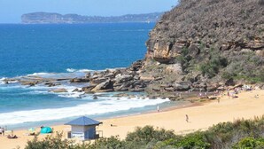 A beach with rocky cliffs, a lifeguard tower, and a clear view of the ocean. - A Beachside Getaway 12 by HolidayCo. (KILLCARE)