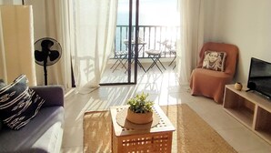 A living room with a sofa, a coffee table with a plant, a TV stand, and a balcony with outdoor furniture. - Opal Moon, Santiago del Teide (Santiago del Teide)