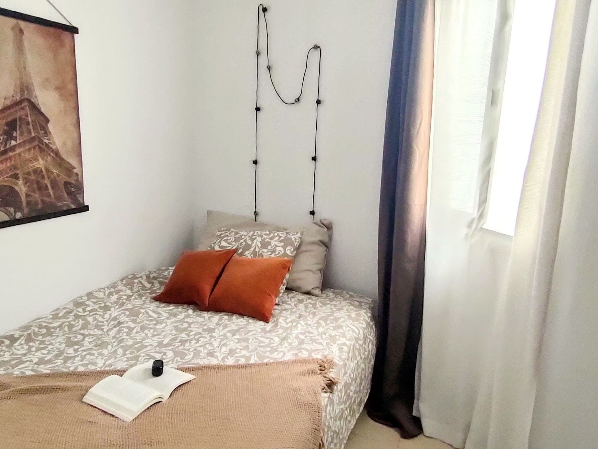 A bedroom with a bed, a book, and a painting of the Eiffel Tower.