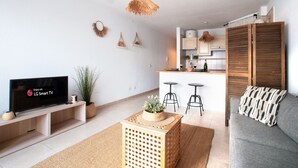 A modern living room with a flat-screen TV, a grey sofa, a wooden coffee table, and a kitchen area in the background. - Opal Moon, Santiago del Teide (Santiago del Teide)