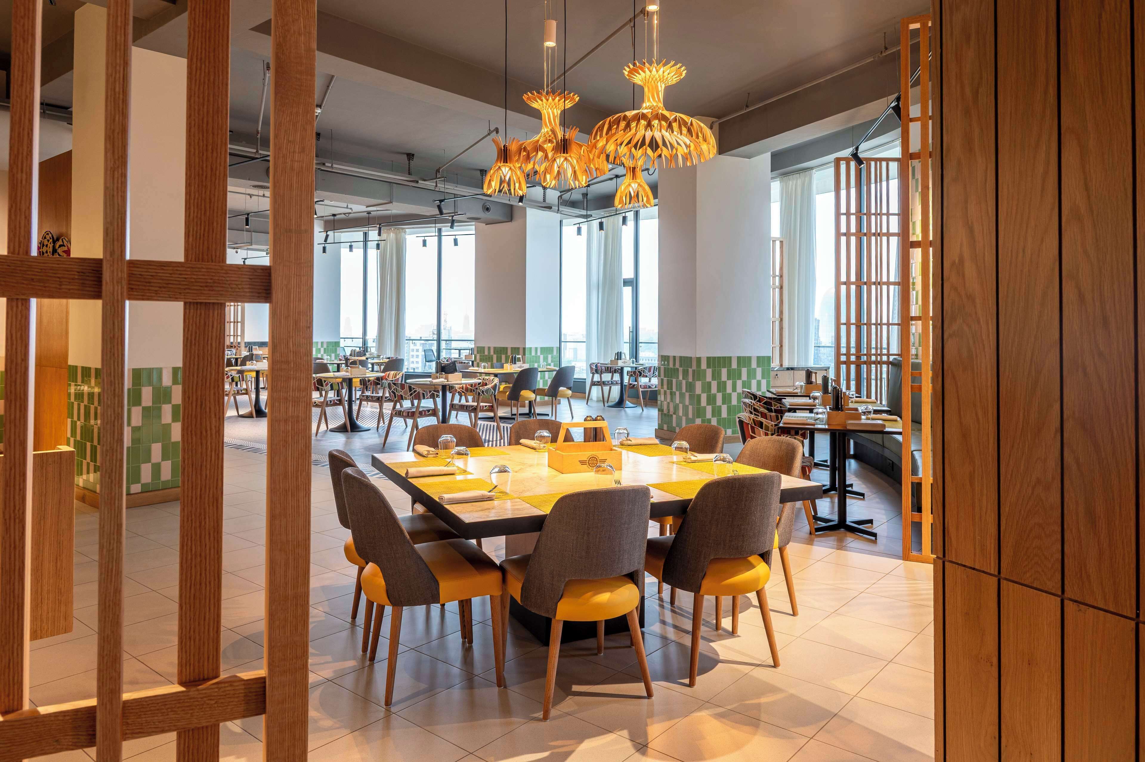 A modern dining area with a large table and chairs, wooden partitions, and hanging pendant lights.