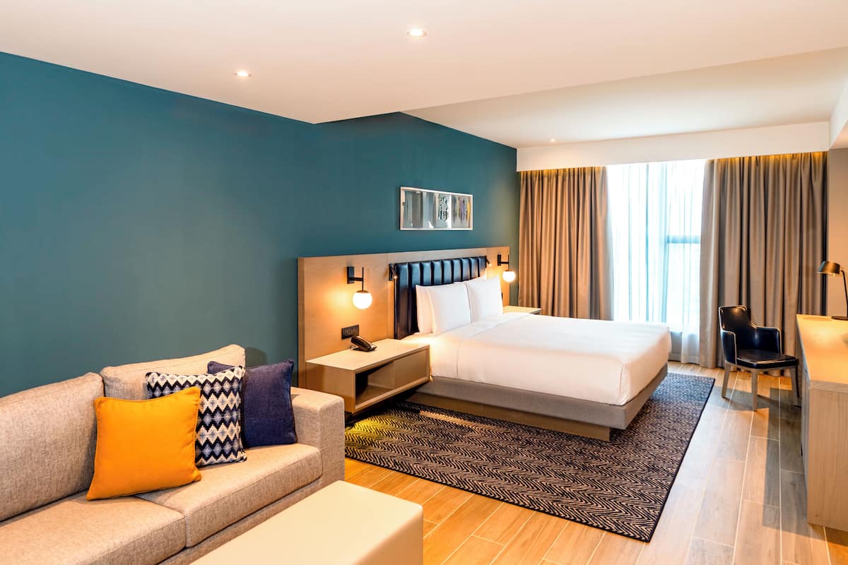 Ein modernes Hotelzimmer mit einem großen Bett, einer Couch, einem Schreibtisch und einem Sessel.