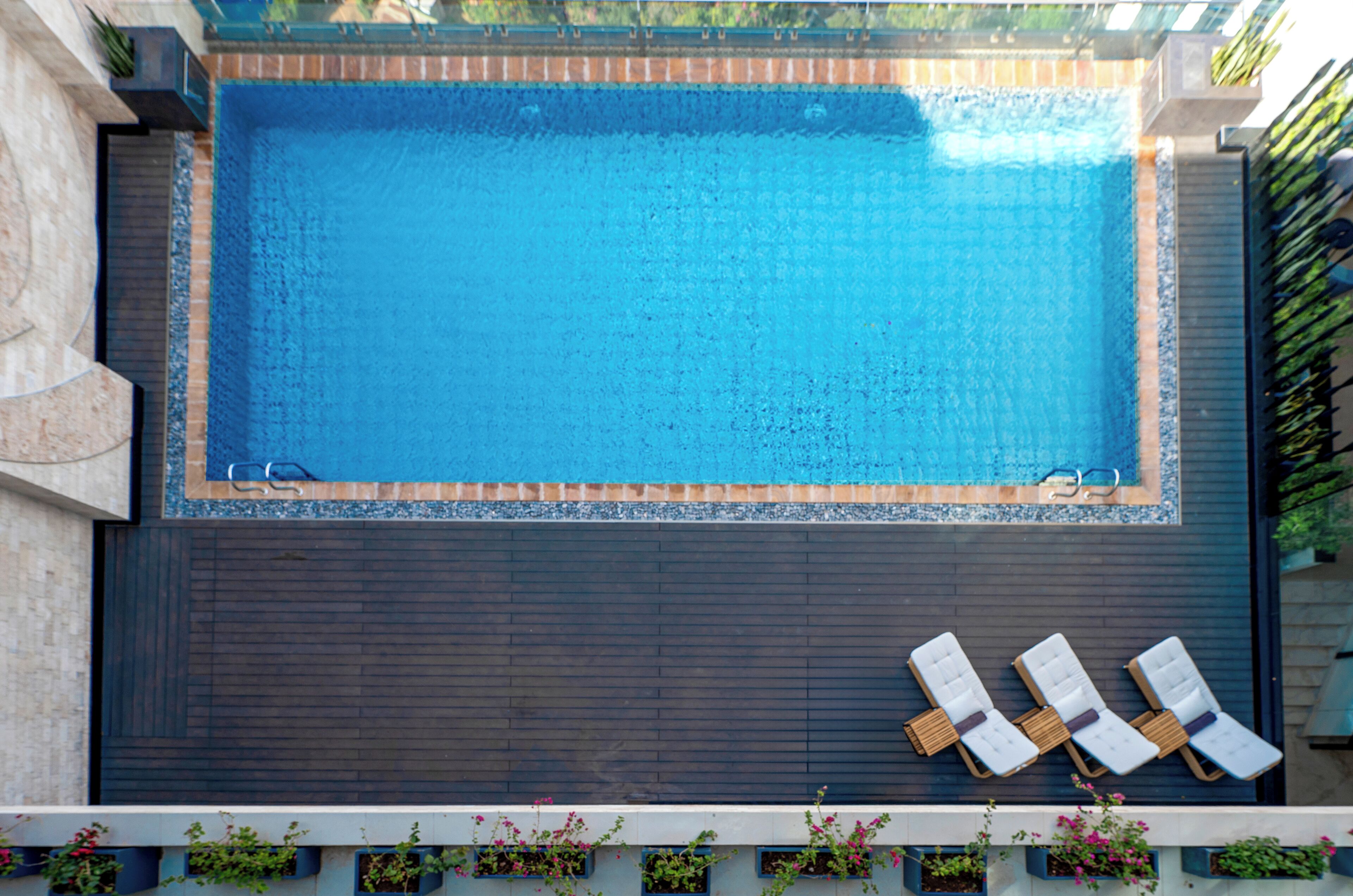 Una piscina rectangular con cubierta de madera oscura y tres sillas reclinables blancas.