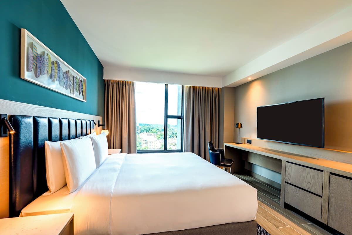 Ein Hotelzimmer mit einem großen Bett, einem Flachbildfernseher, einem Schreibtisch und einem fenster mit Vorhängen.