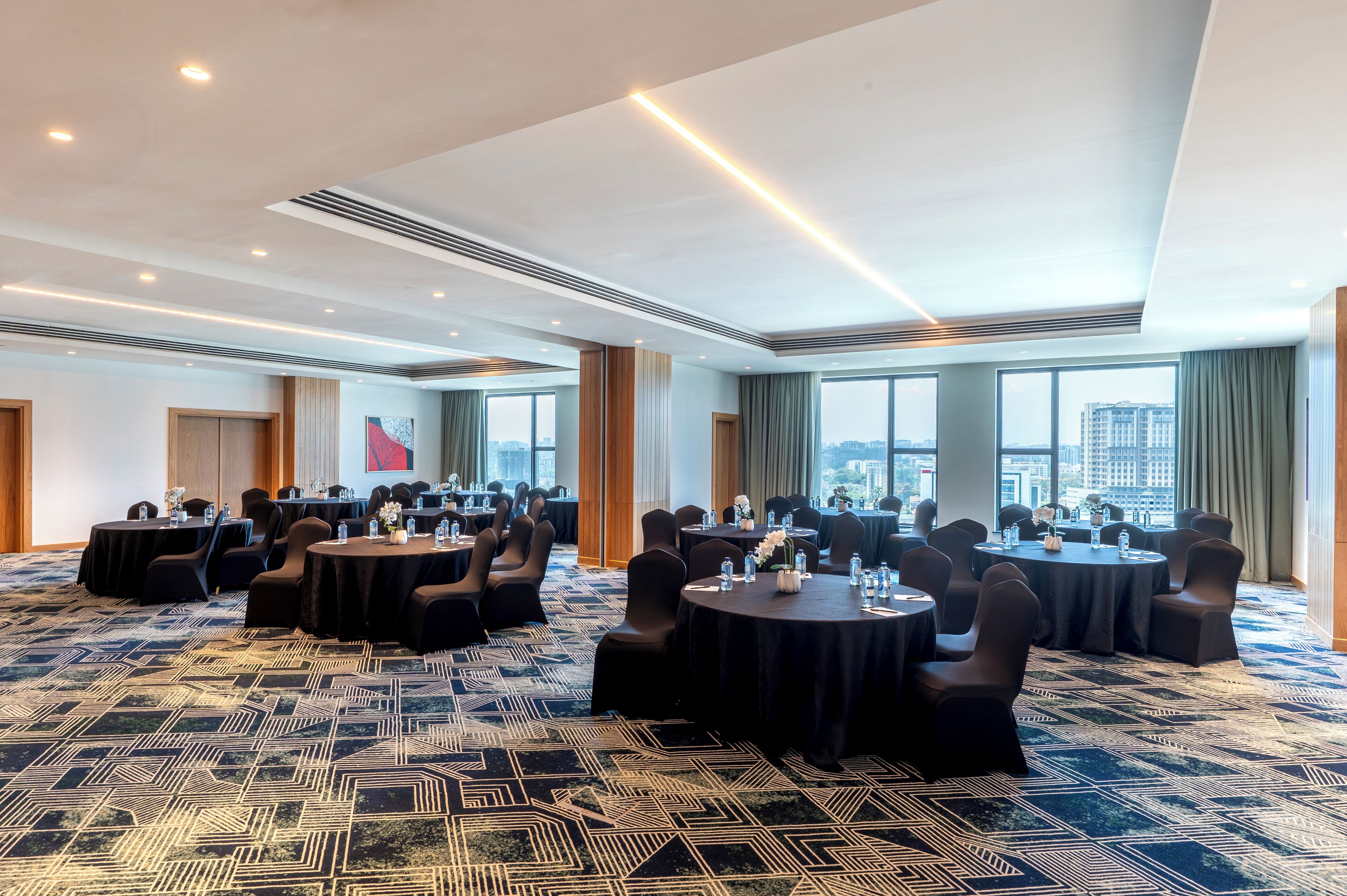 Un salón de conferencias con mesas redondas, sillas y una alfombra estampada.