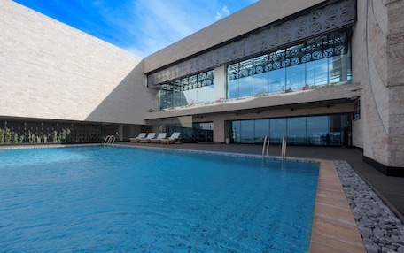 A modern building with a swimming pool, sun loungers, and a glass facade.