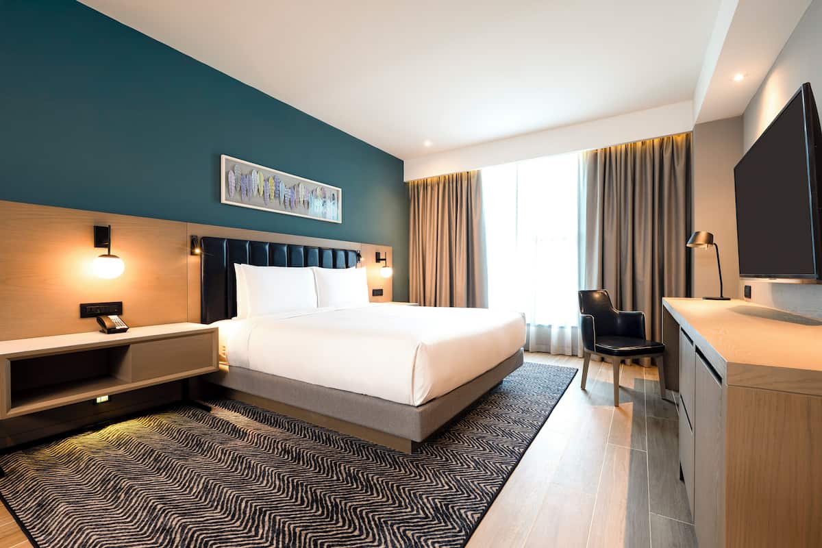 Ein modernes Hotelzimmer mit einem großen Bett, einem Schreibtisch, einem Sessel, einem Flachbildfernseher und einem Badezimmer.