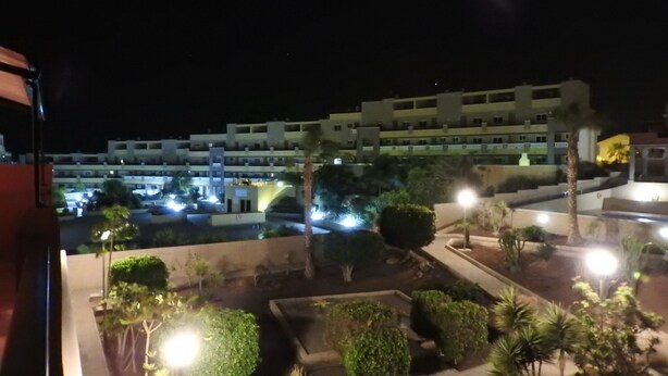 A nighttime view of a hotel courtyard with illuminated pathways, a pool, and a multi-story building in the background. - CM 2 bd near the sea (El Médano)