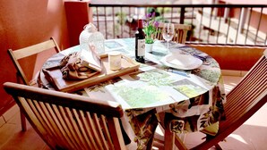 A round table set for two with a patterned tablecloth, a wine bottle, a candle, and a glass on a balcony with a view of buildings. - CM 2 bd near the sea (El Médano)