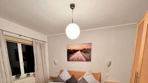 A modern bedroom with a wooden bed, a view of the sunset through the window, and a wooden wardrobe. - Ferienwohnung Baalmann Nr. 2 (Borkum)