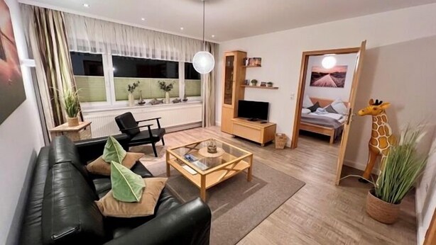 A modern living room with a black leather sofa, a glass coffee table, a TV stand, and a giraffe decoration. - Ferienwohnung Baalmann Nr. 2 (Borkum)