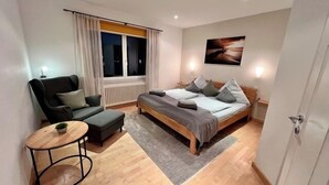 A modern bedroom with a bed, a chair, a small table, and a window. - Ferienwohnung Baalmann Nr. 4 (Borkum)