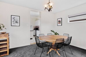 Een eetgedeelte met een ronde houten tafel, zwarte draadframe stoelen, een kroonluchter en lijstwerken aan de wanden.