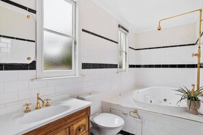 Een badkamer met een wit wastafelmeubel, toilet en badkuip, met zwart-wit tegels en gouden sanitair.