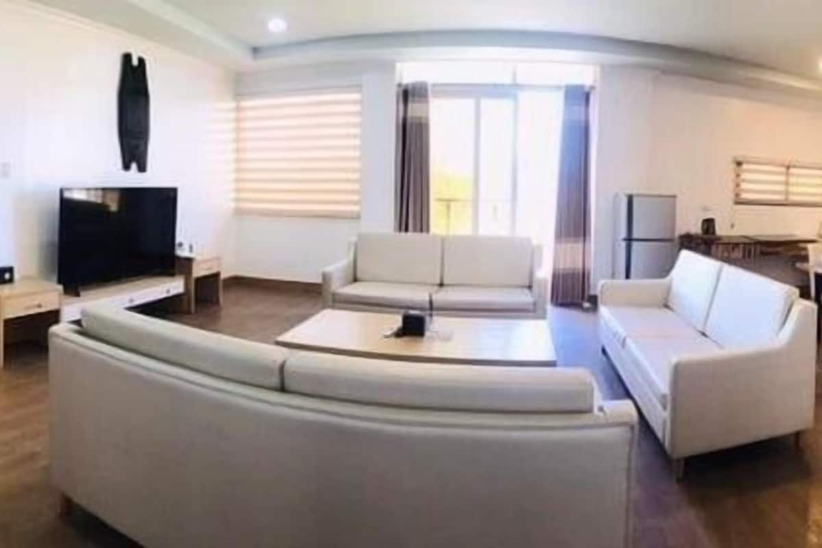 A modern living room with a curved sofa, a flat-screen TV, and a dining area with a table and chairs.