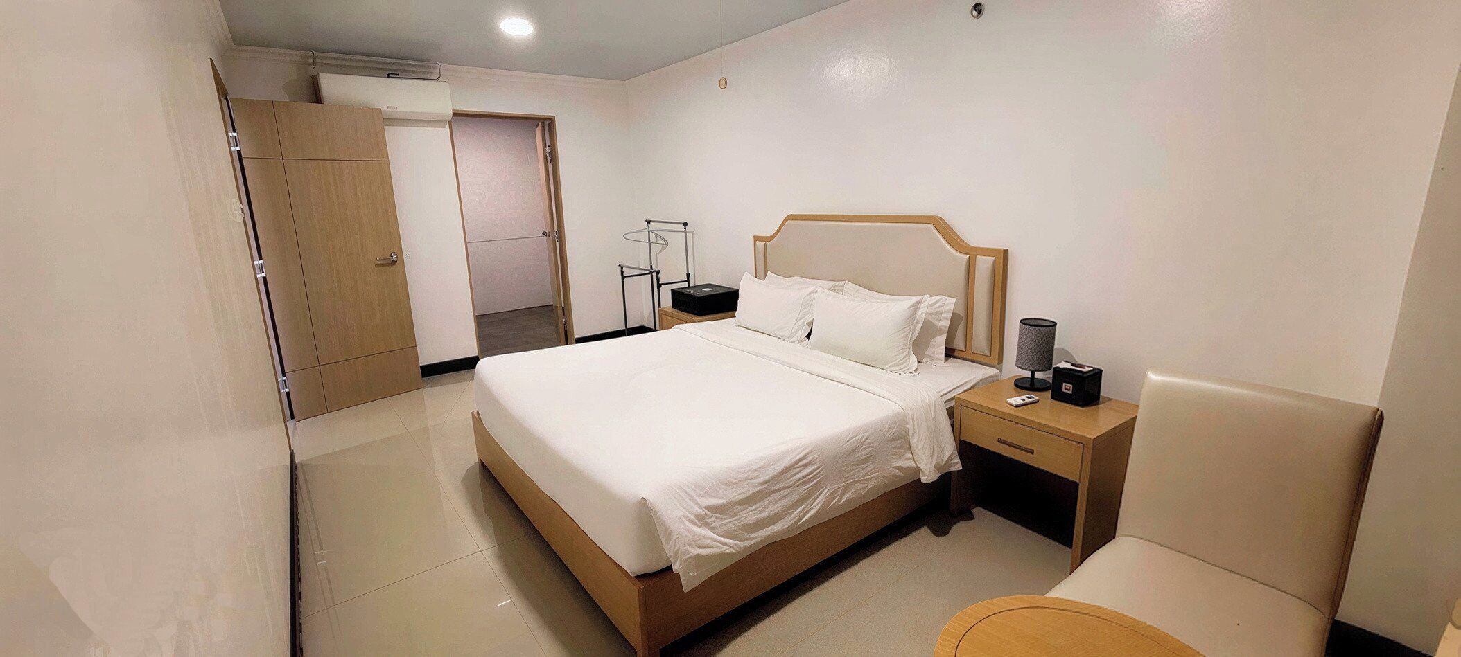 Una habitación de hotel con cama, mesita de noche, lámpara y armario.