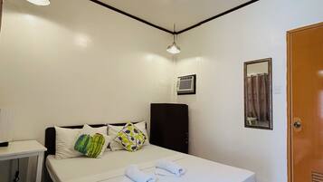 A hotel room with a bed, bedside table, lamp, air conditioning unit, and a door.