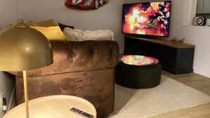 Een woonkamer met een bruine leren bank, een ronde salontafel, een vloerlamp, een televisie en een wandplank met een automodel.