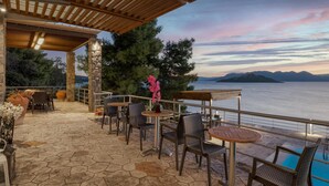 Eine Terrasse im Freien mit Steinböden, Korbmöbeln und Blick aufs Meer.