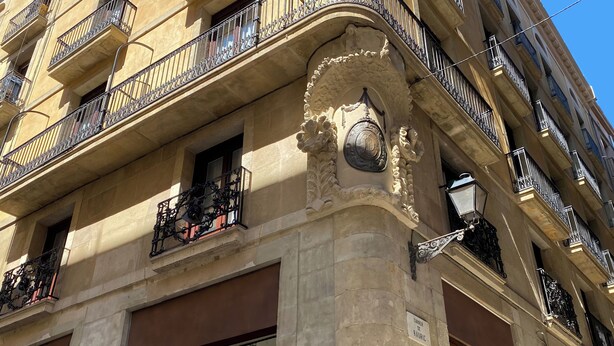 A corner of a building with ornate balconies, a large window, and a street lamp. - Casa Pince (Barcelona)