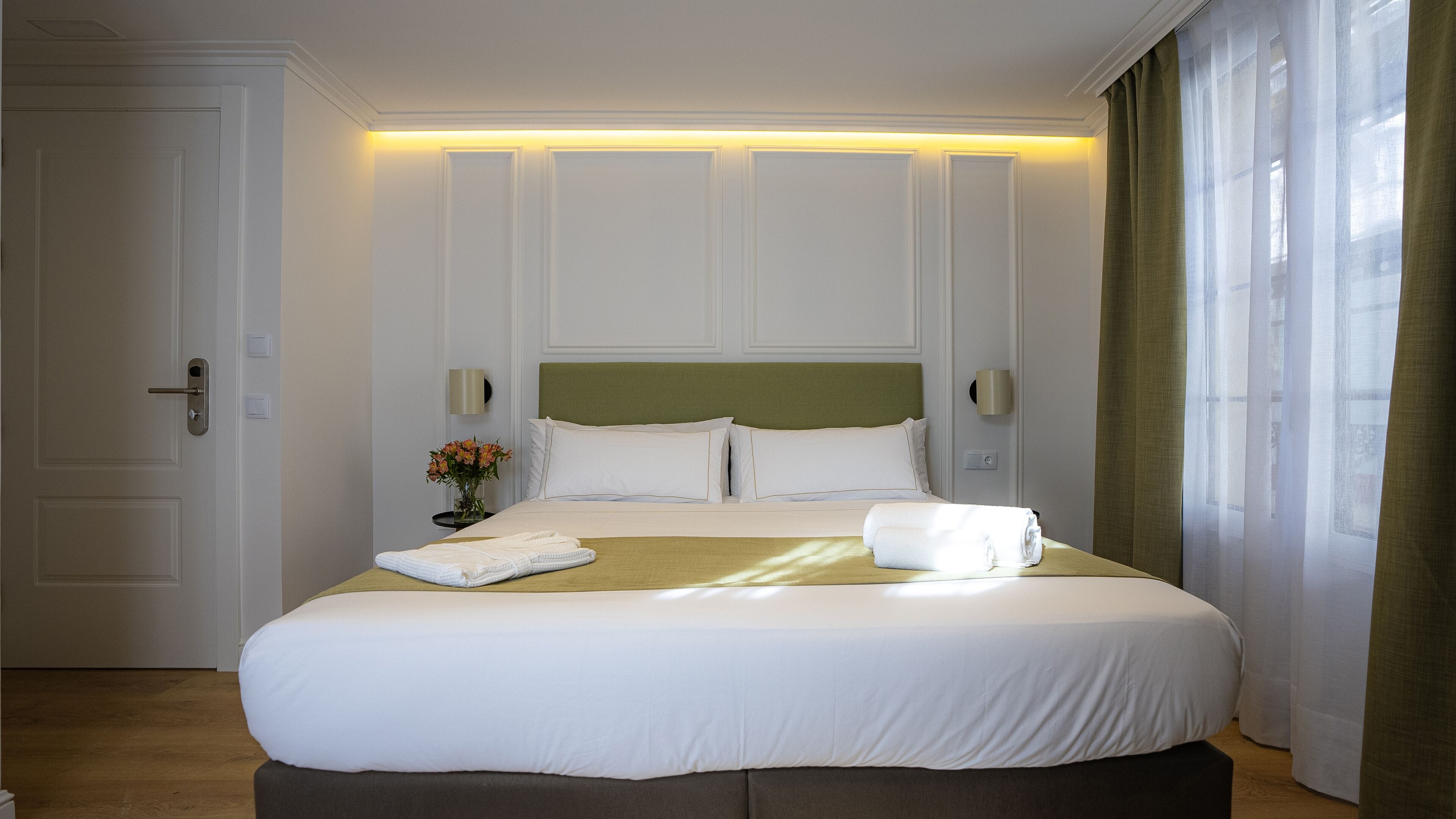Ein Hotelzimmer mit einem großen Bett, einem Nachttisch mit Blumenvase und einer Tür.