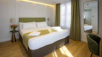Ein Hotelzimmer mit einem großen Bett, einem Nachttisch mit Lampe, einem Spiegel und einem grünen Sessel.
