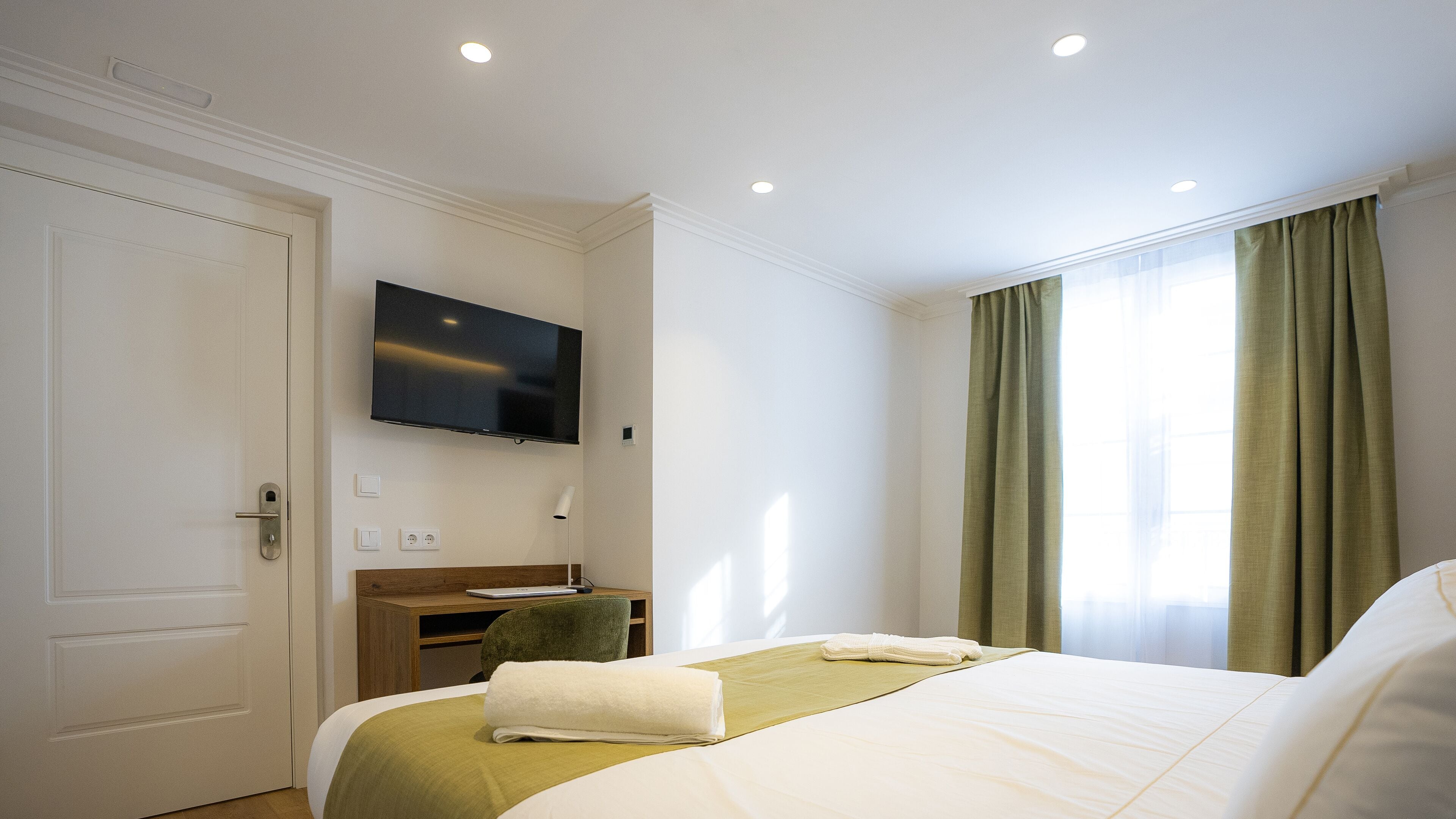 A hotel room with a bed, a desk, a television, and a window with curtains.