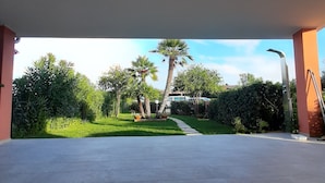 Een open terras met betegelde vloer, omringd door groen en palmbomen.