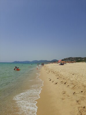 Een strand met helder water, mensen die wandelen en parasols.