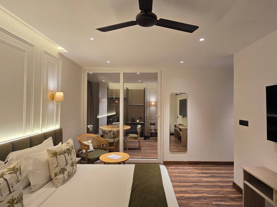 A modern hotel room with a bed, a seating area with a table, a television, and a ceiling fan.