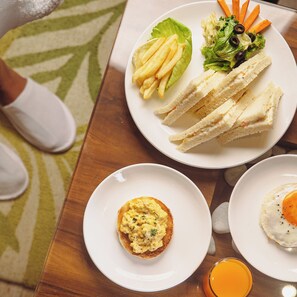 Una mesa con un plato de sándwiches, papas fritas y ensalada, un plato de huevos revueltos y un vaso de jugo de naranja.
