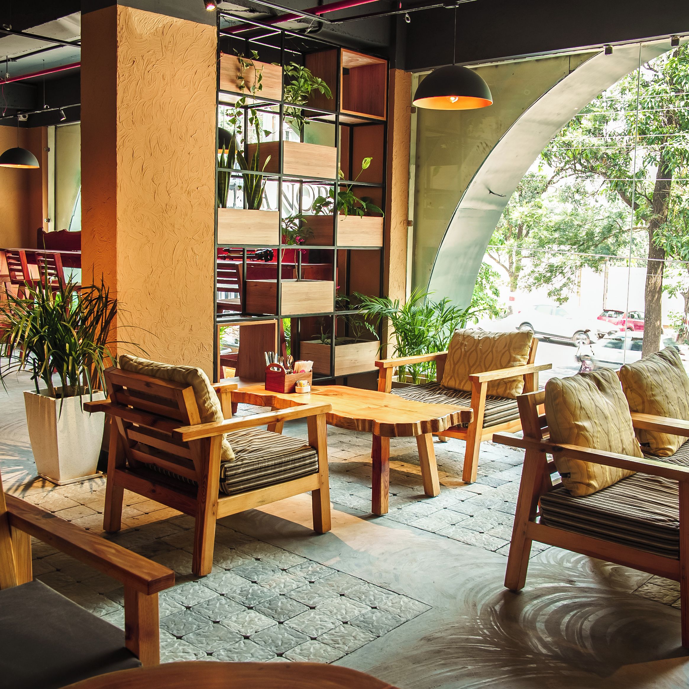 Un acogedor interior de cafetería con muebles de madera, una pared cubierta de plantas y vistas a la calle.