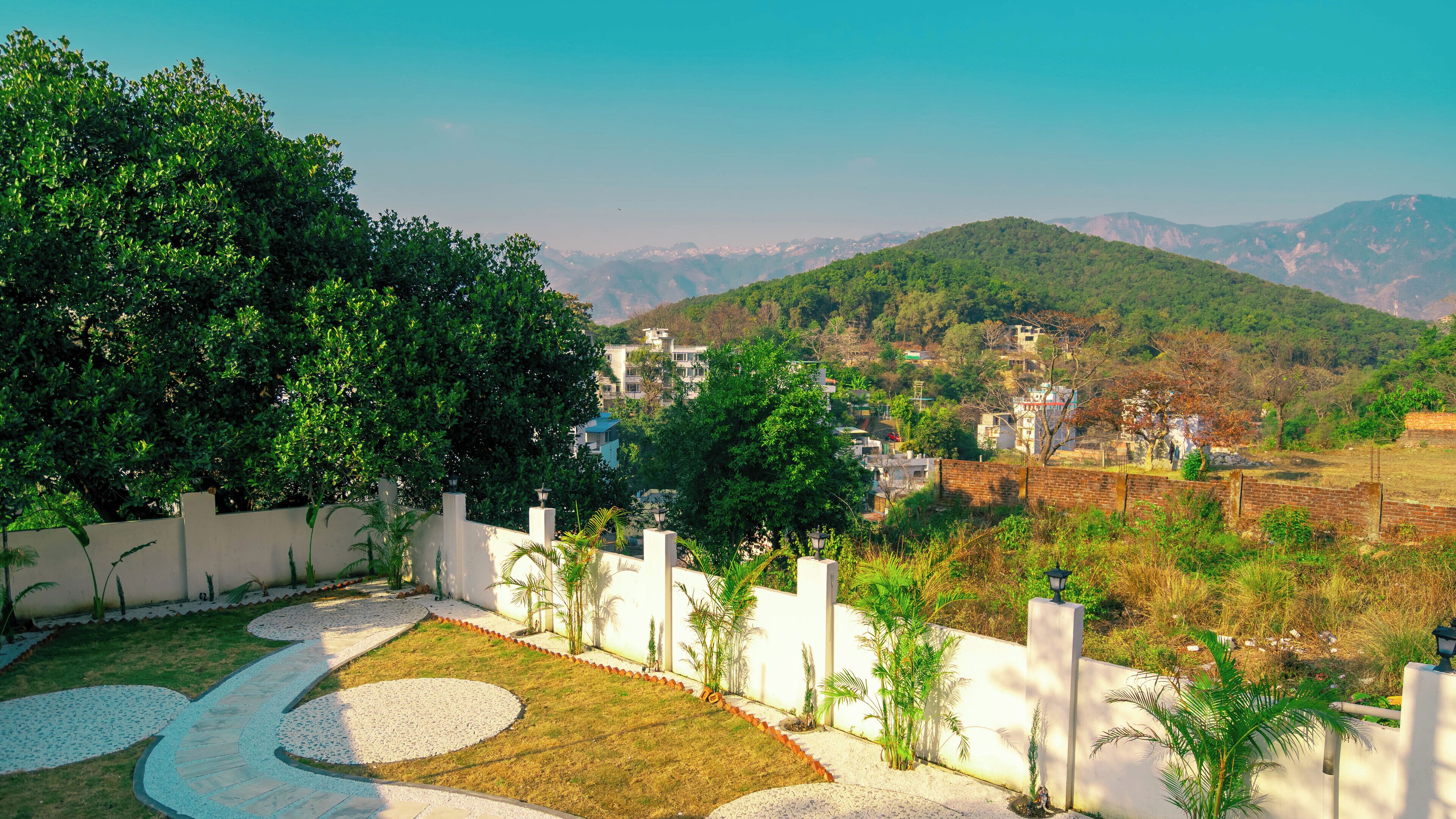 Una zona residencial con un camino de jardín empedrado, paredes blancas y abundante vegetación.