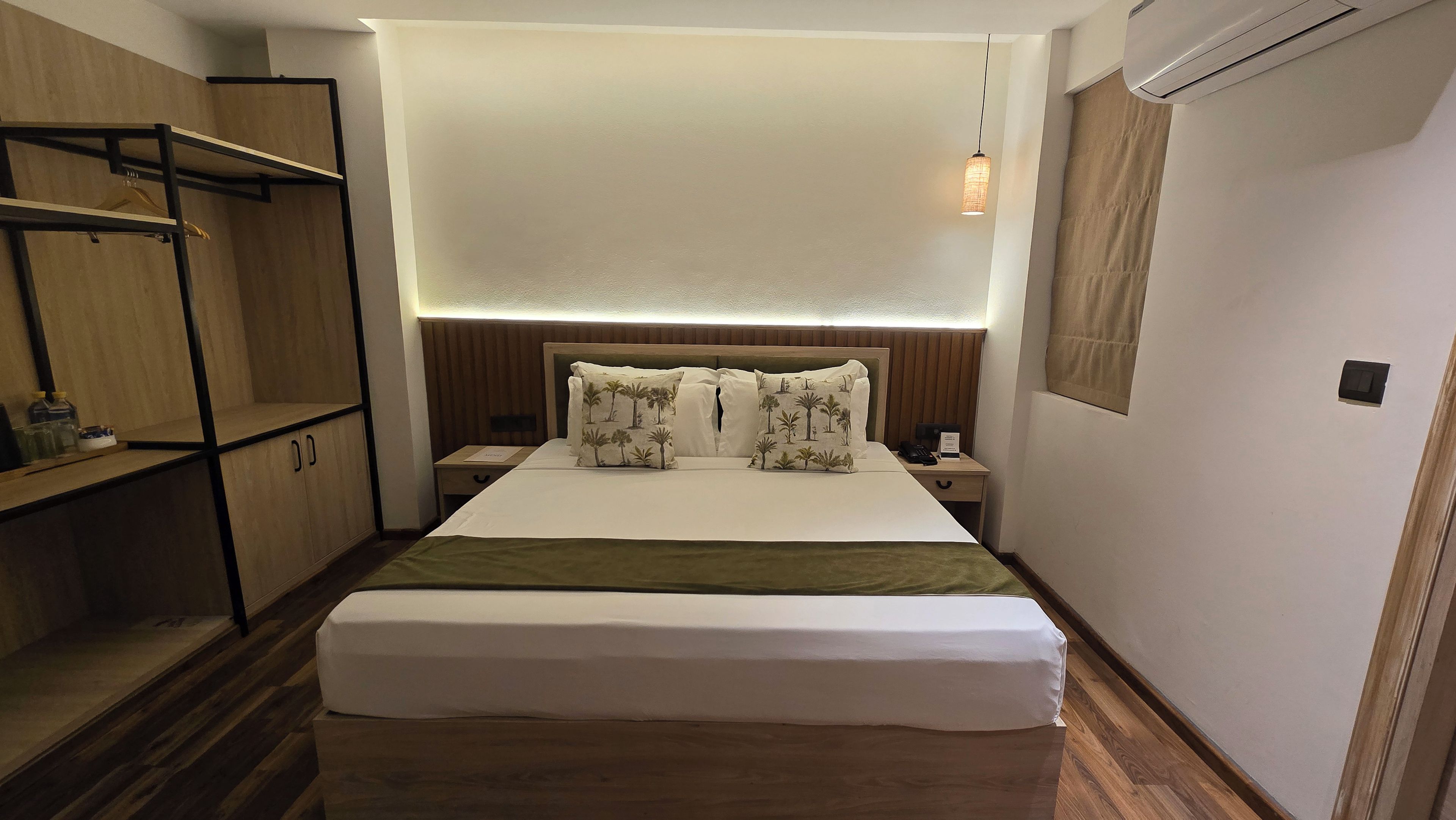 Una habitación de hotel con cama, mesita de noche, armario y lámpara colgante.