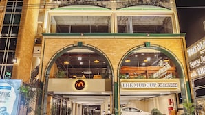 A multi-story building with a prominent entrance, balconies, and a cafe named "The Mudcup Cafe & Dine" at the ground level. - The Manor House Boutique Stays (Dehradun)