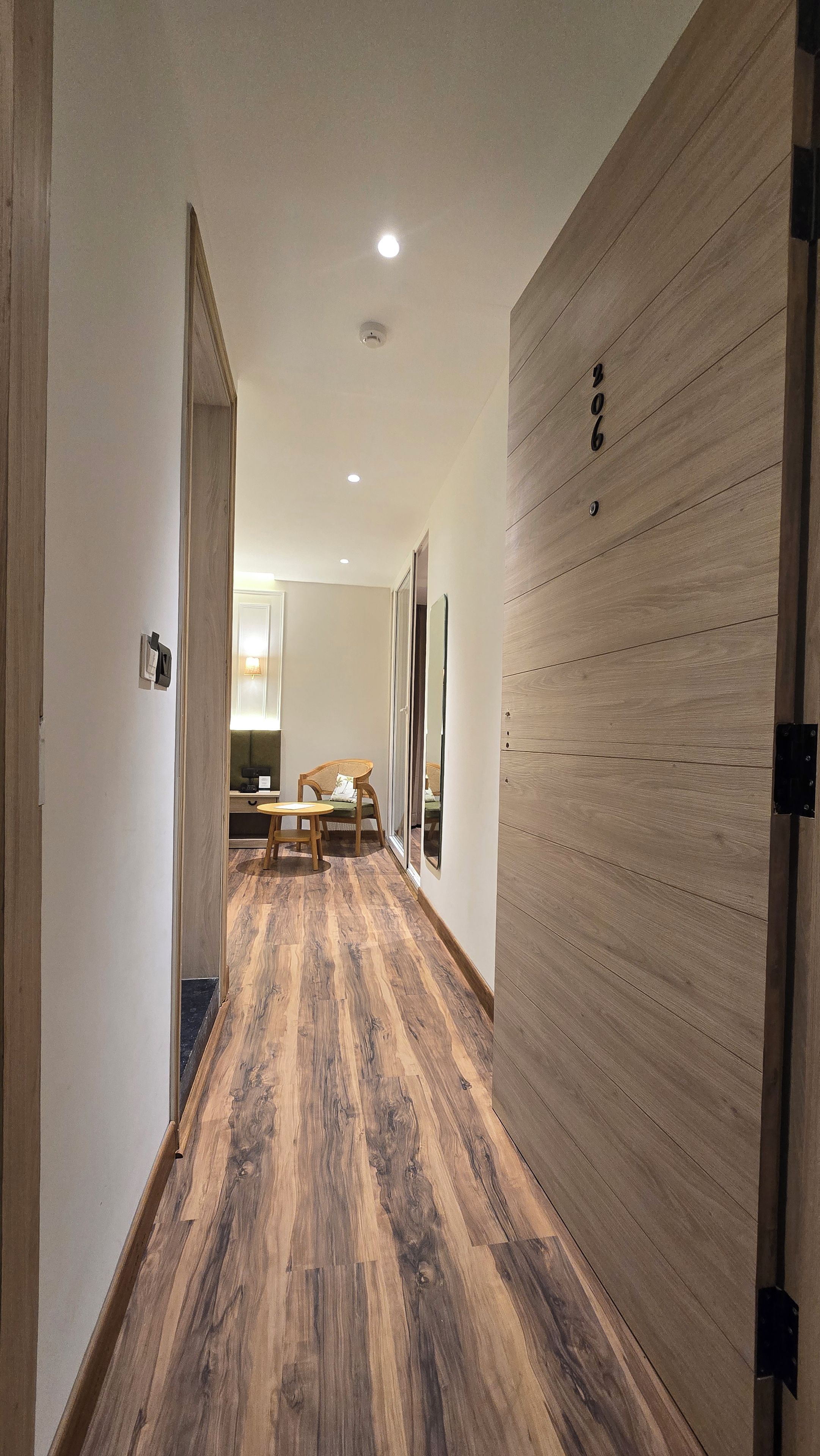 A hallway with wooden flooring, a sliding door with a number, and a seating area with a table and chairs.