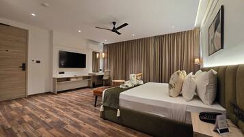 Habitación de hotel con cama, escritorio, televisión, ventilador de techo y un ventanal con cortinas.