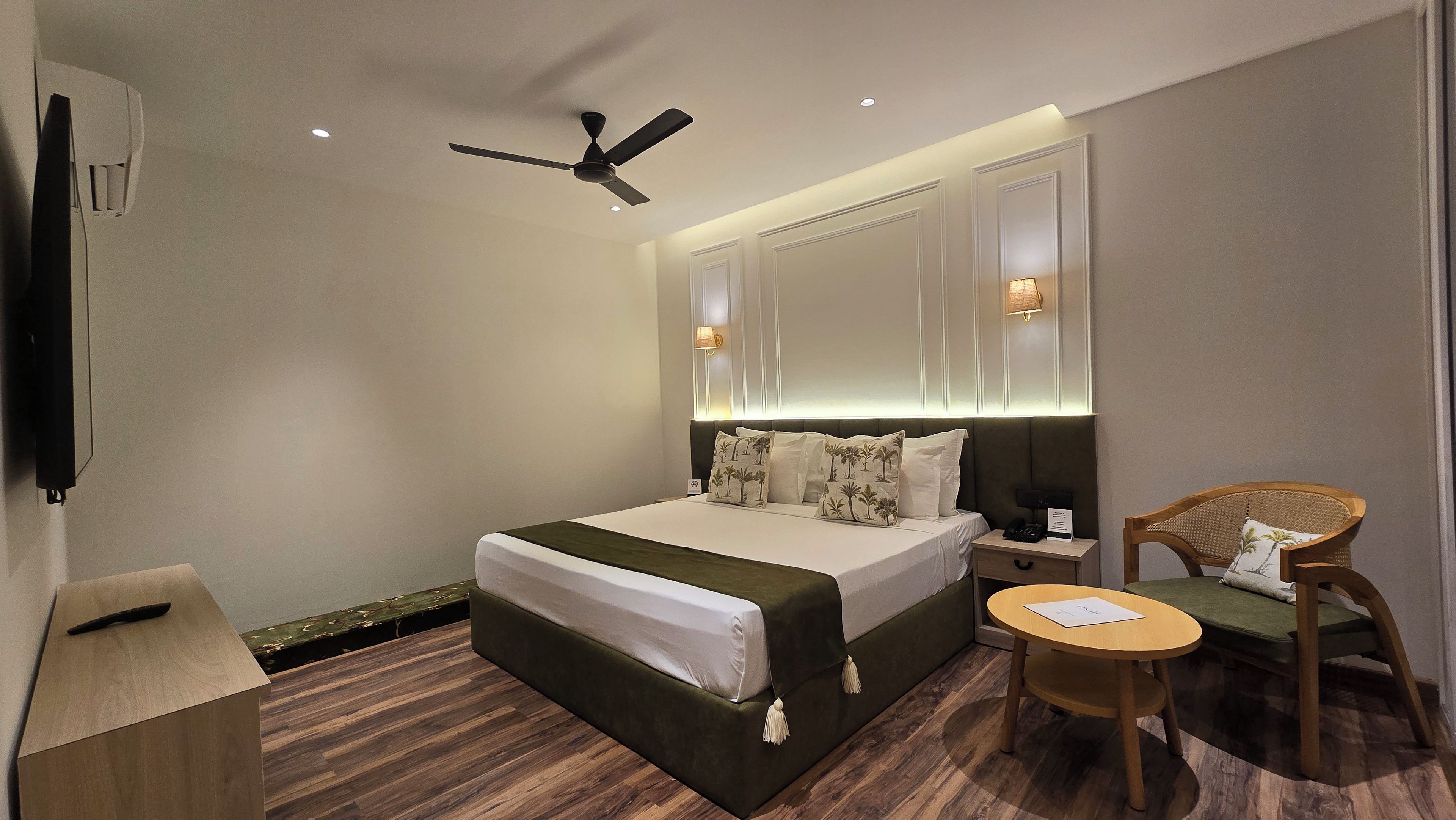Habitación de hotel con cama, mesita de noche, silla y ventilador de techo.
