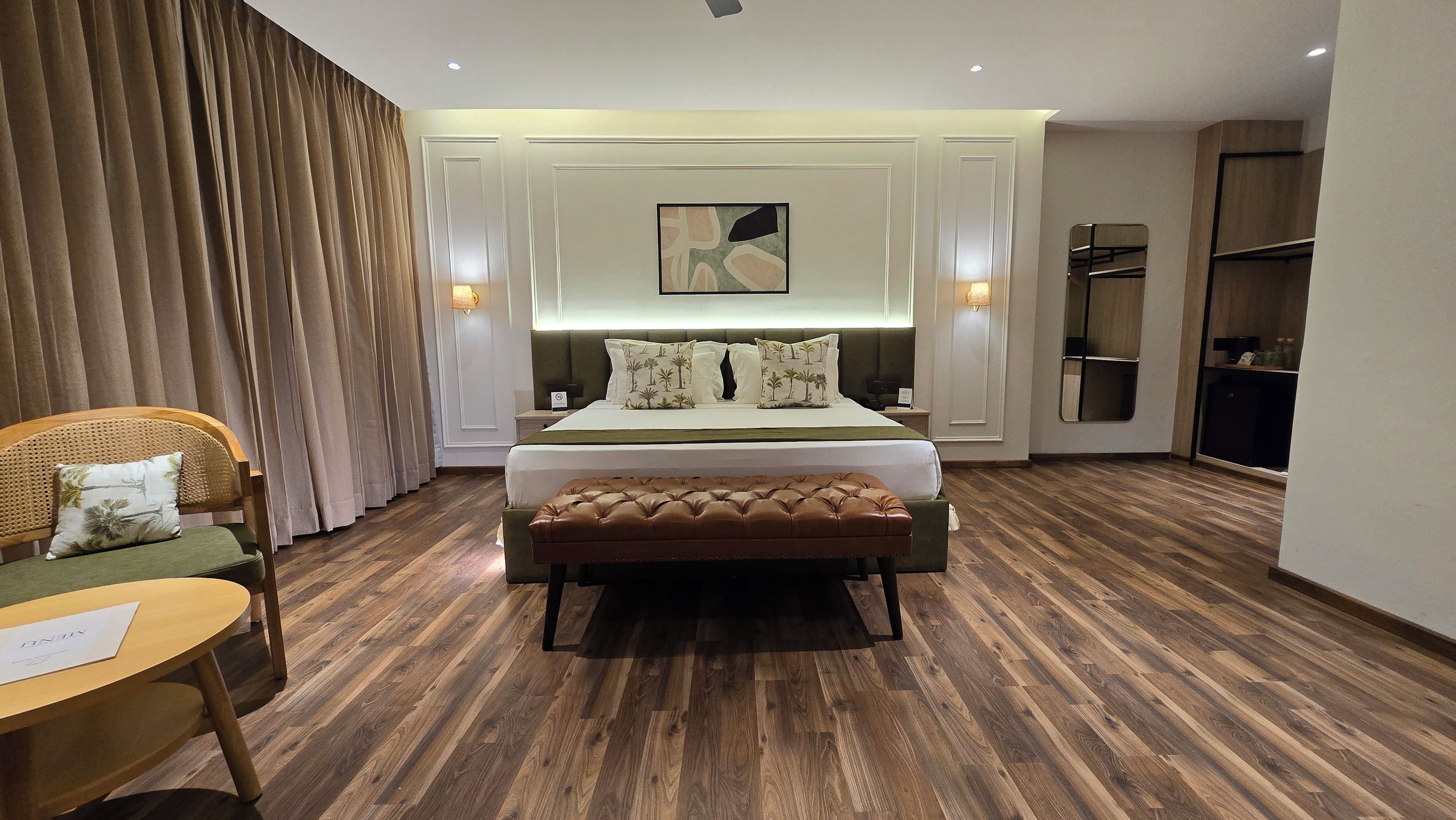 A hotel room with a bed, a bench, a chair, a desk, and a wardrobe.