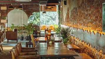 A restaurant interior with wooden tables and chairs, brick walls, and hanging pendant lights.
