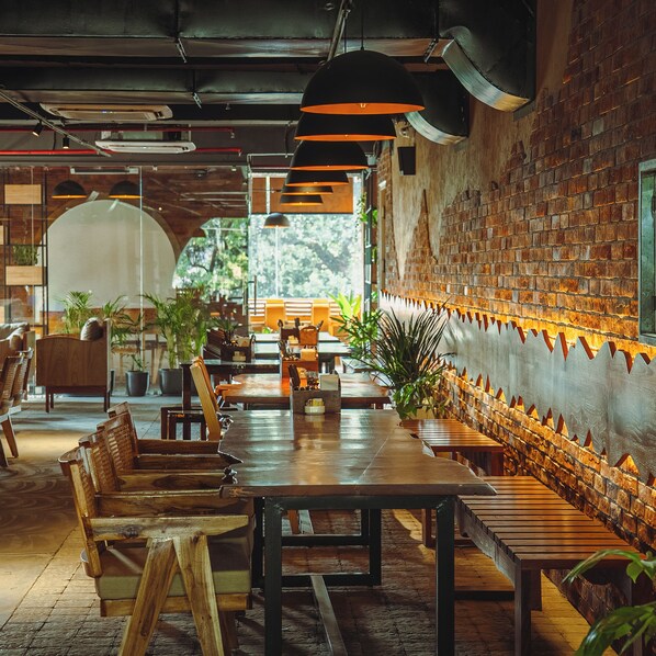 Un interior de restaurante con mesas y sillas de madera, paredes de ladrillo y lámparas colgantes.