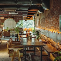 Un interior de restaurante con mesas y sillas de madera, paredes de ladrillo y lámparas colgantes.