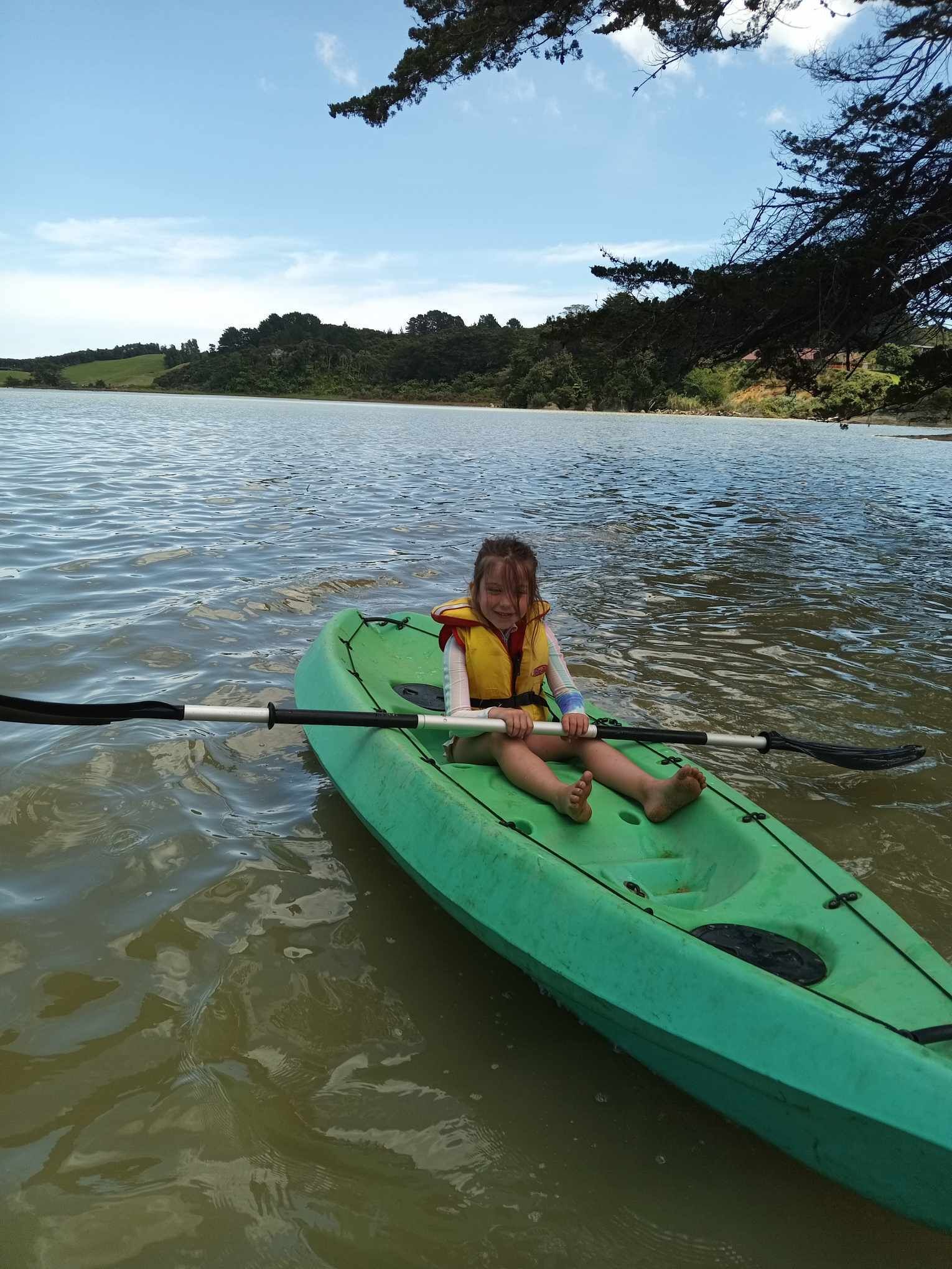 A person in a green kayak on a body of water with a forested shoreline in the background.