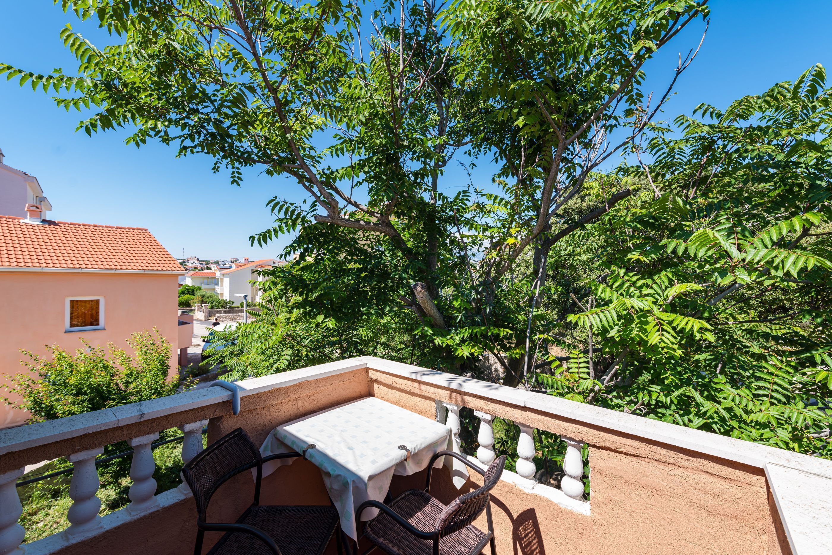 A balcony with a table and chairs, surrounded by greenery and buildings.