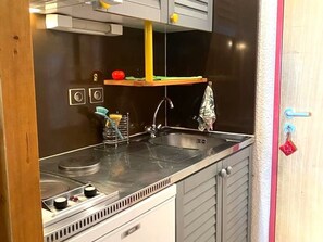 Une cuisine équipée d’un évier, d’une cuisinière et d’une petite étagère sur laquelle se trouve une tomate.