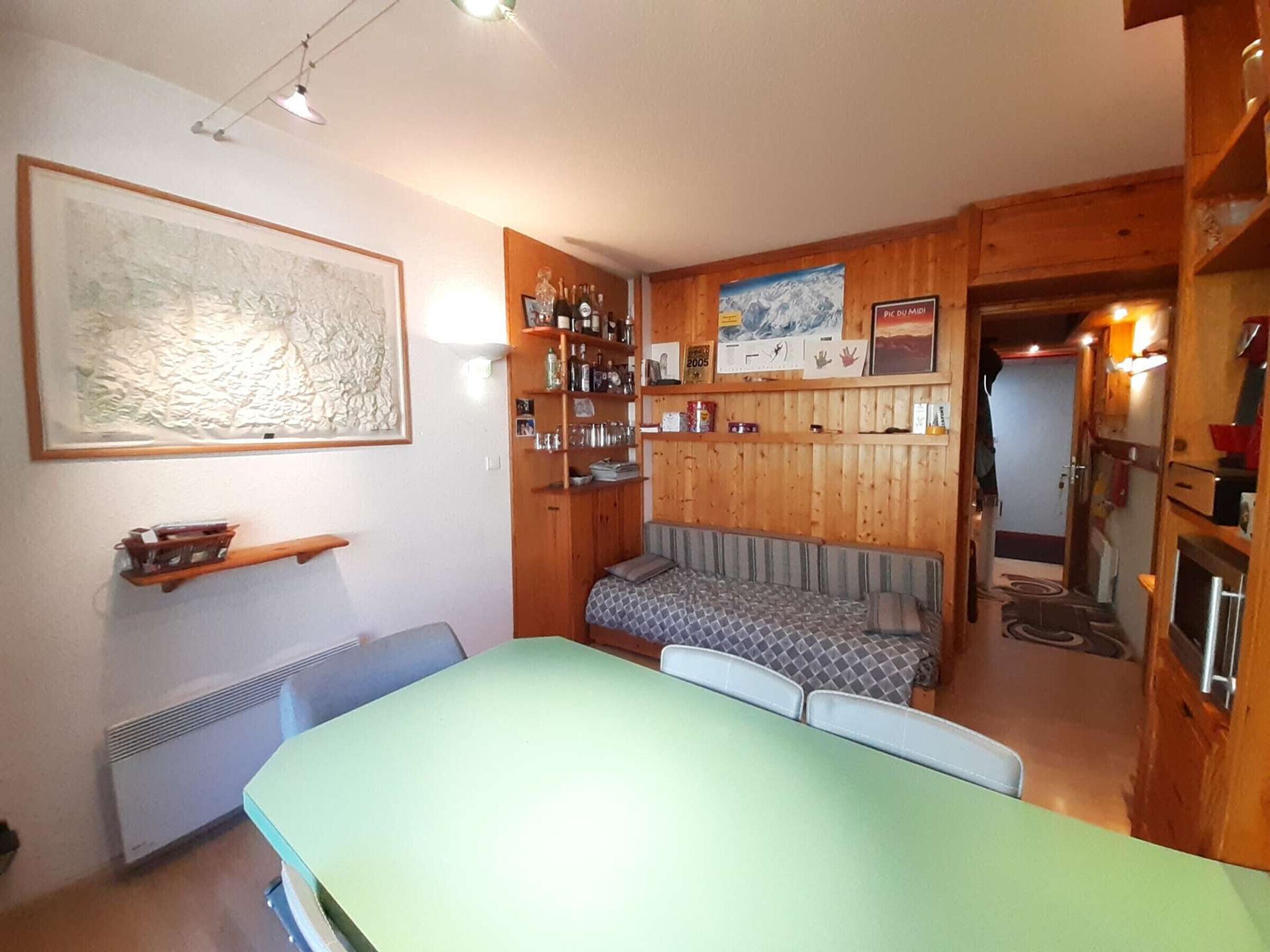 A cozy room with a green table, a sofa, and a wooden wall with shelves.