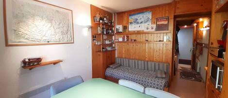 A cozy room with a green table, a sofa, and a wooden wall with shelves.